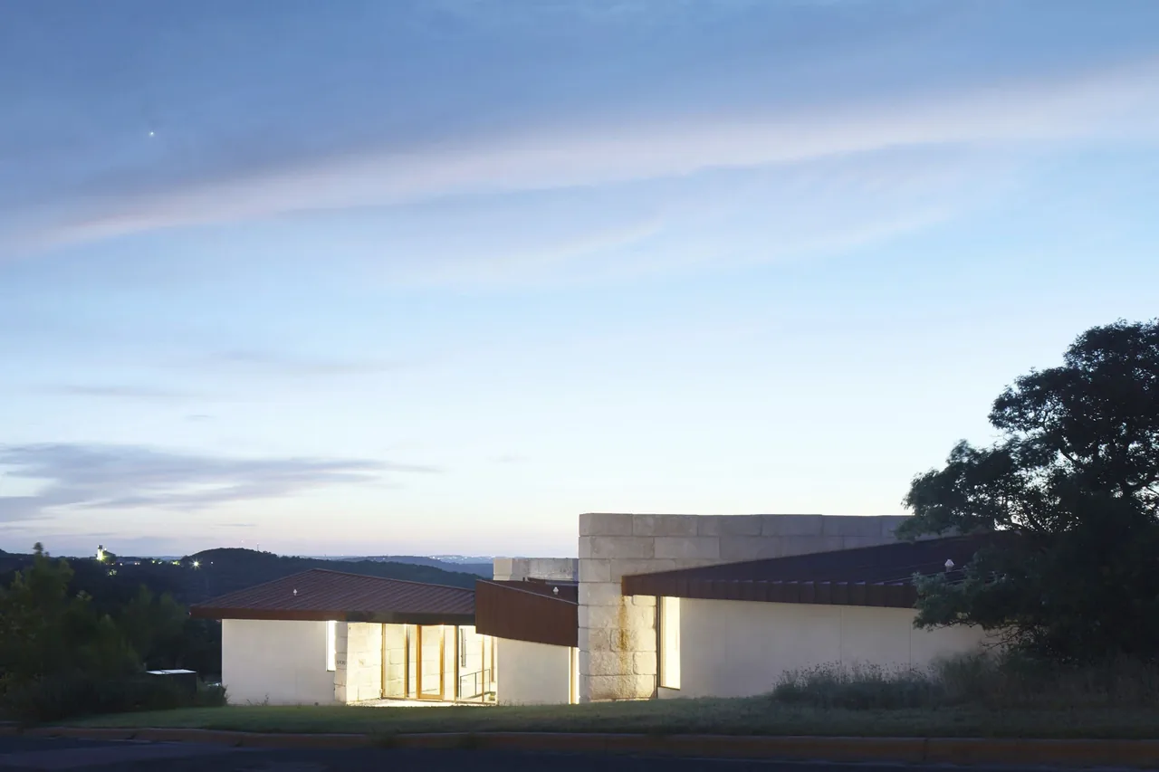 Bold Ruler House features a modern design with flat roofs and stone walls, situated in a natural setting at dusk.
