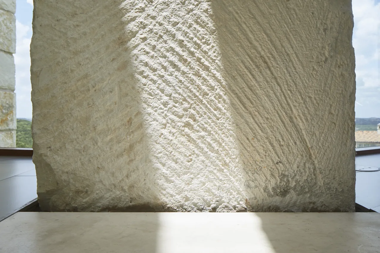 Textured stone wall inside the Bold Ruler House, illuminated by natural light and casting shadows on the floor.