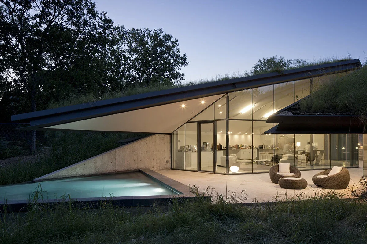 The Bold Ruler House features sloped green roofs, a glass wall facade, and a reflecting pool integrated into the landscape.