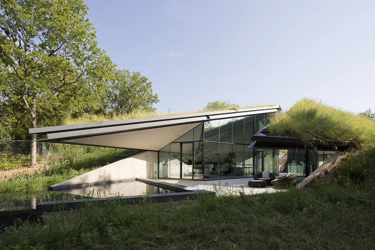 Bold Ruler House features floor-to-ceiling glass walls and sloped green roofs with an outdoor seating area.