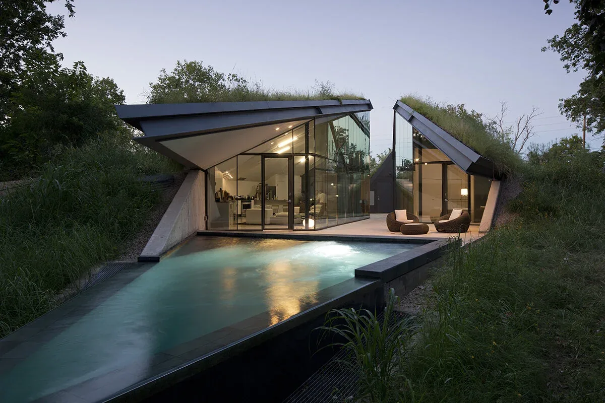 Bold Ruler House features sloped green roofs, extensive glass wall facades, and a reflecting pool integration by Bercy Chen Studio in Austin.