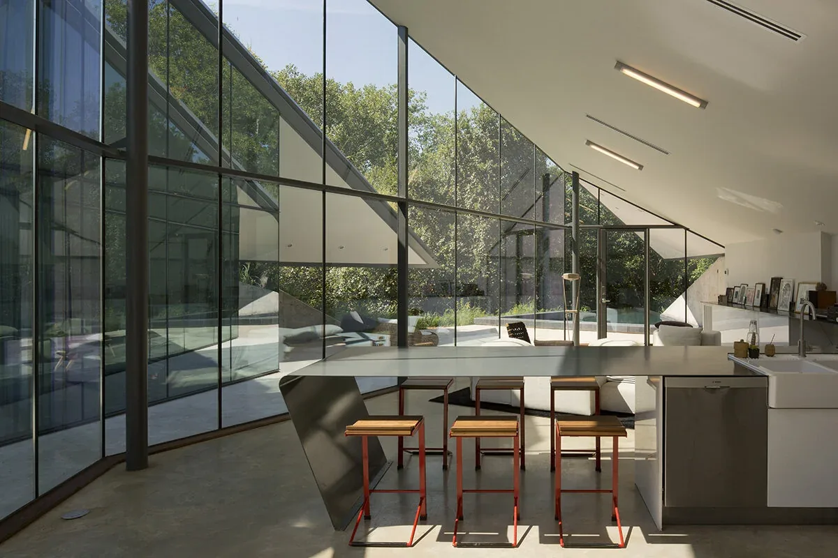 Bold Ruler House kitchen with floor-to-ceiling glazing and an angular roof design visible through the glass walls.