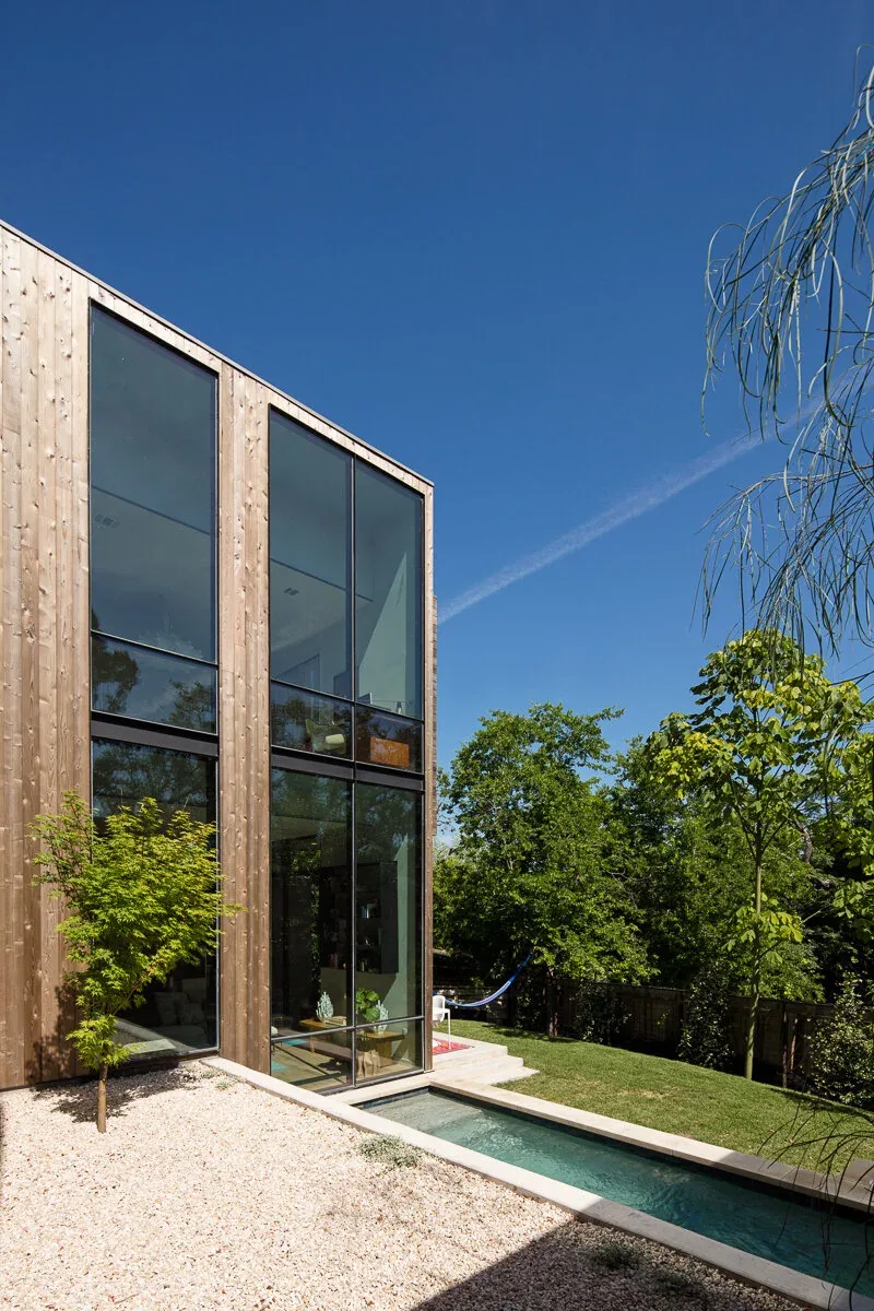 Edgeland House features vertical wood siding with floor-to-ceiling windows and a small reflecting pool outside.
