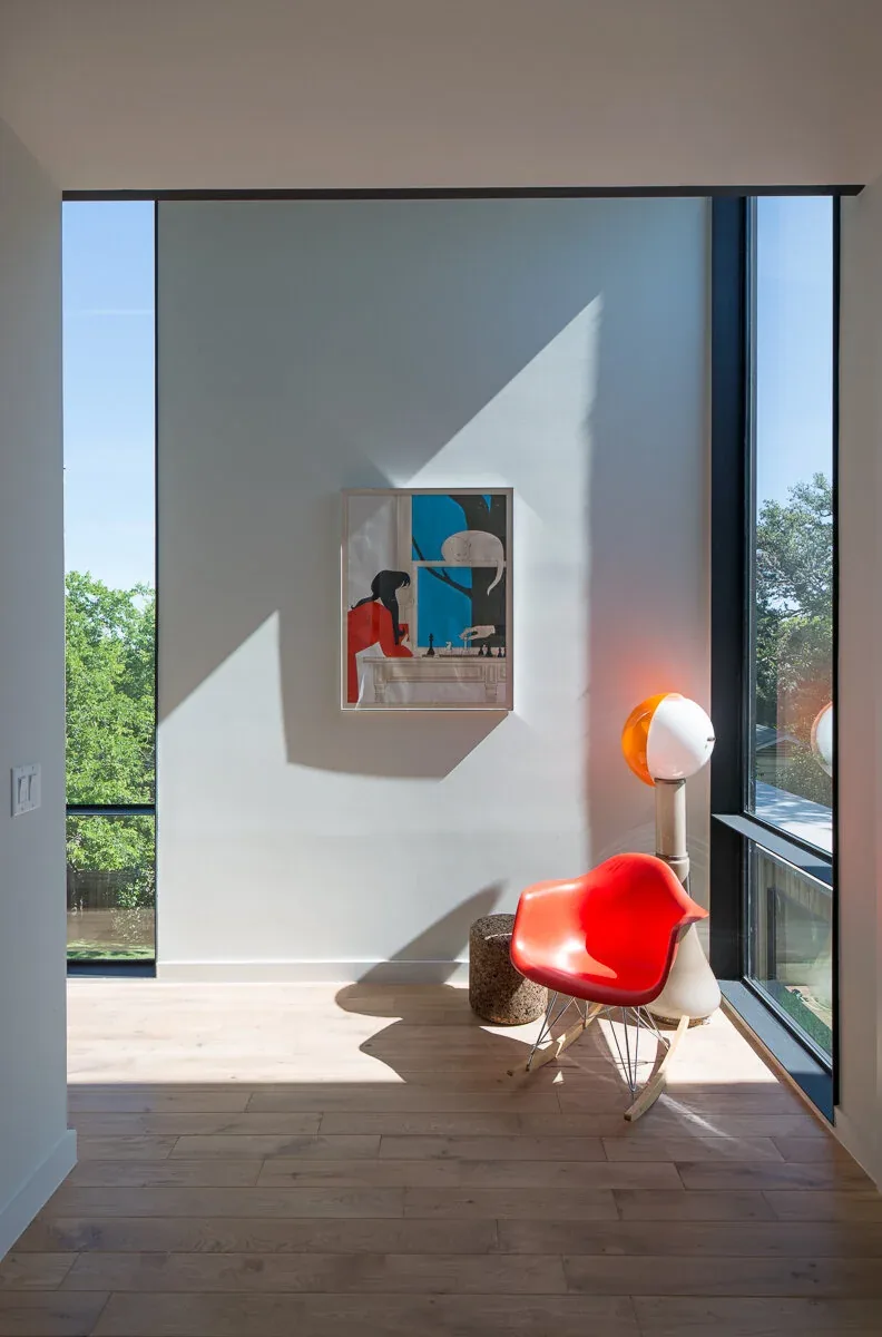 A bright sitting nook features floor-to-ceiling glazing, a red rocking chair, and abstract wall art in the Edgeland House.