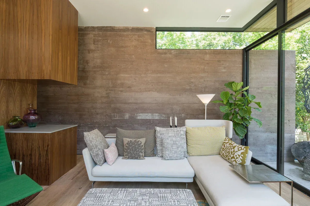 Living room space features a white sofa with multiple pillows, a green chair, and a board-formed concrete accent wall next to floor-to-ceiling glazing.