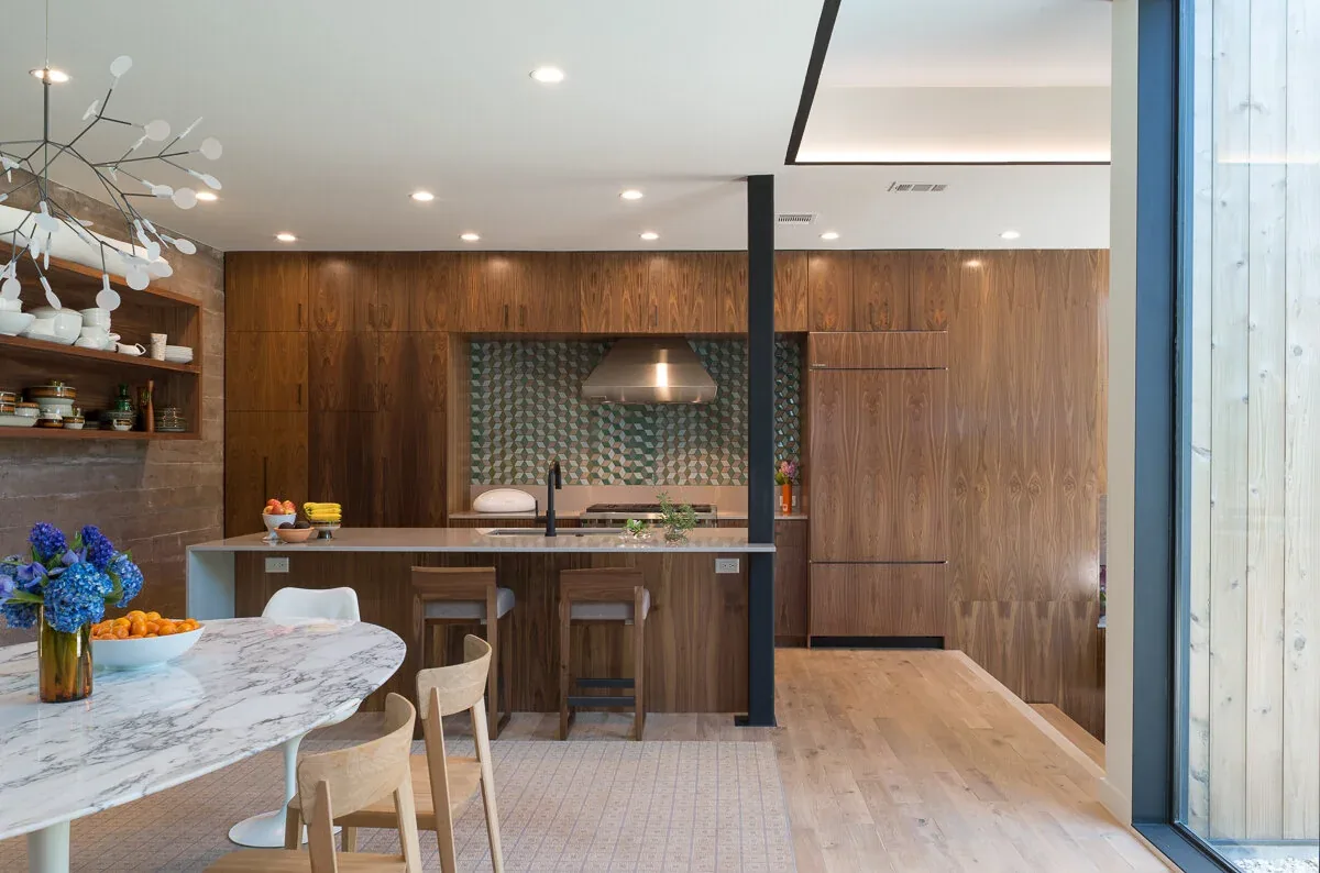 Edgeland House kitchen features walnut cabinetry with a patterned tile backsplash and a marble dining table with wooden chairs.
