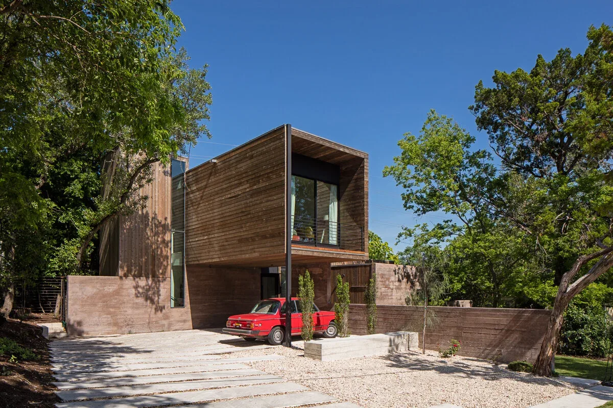 The Edgeland House features vertical wood siding and concrete walls with a carport beneath an upper cantilevered volume.