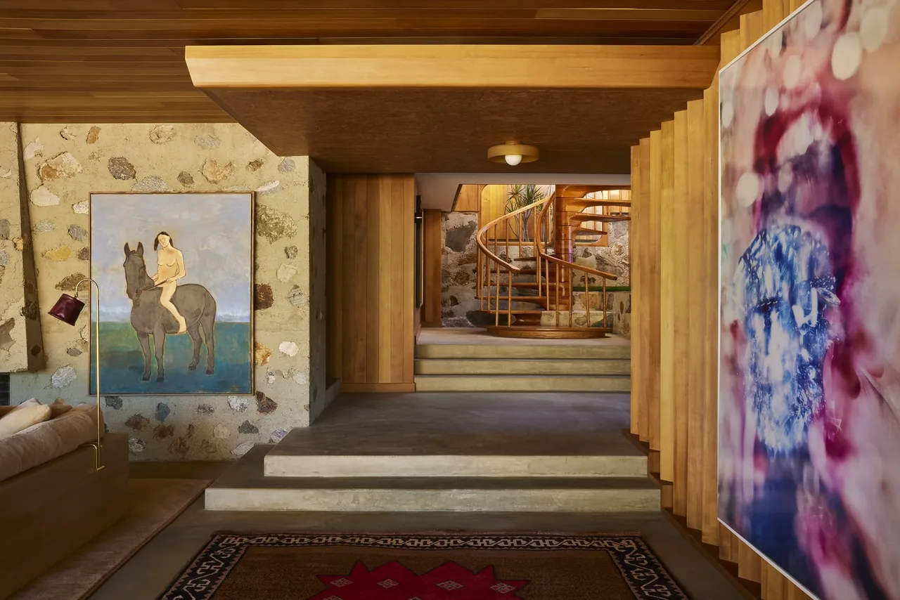 The Claremont residence features a wooden spiral staircase within a stone-walled room accented by artwork and wood paneling.