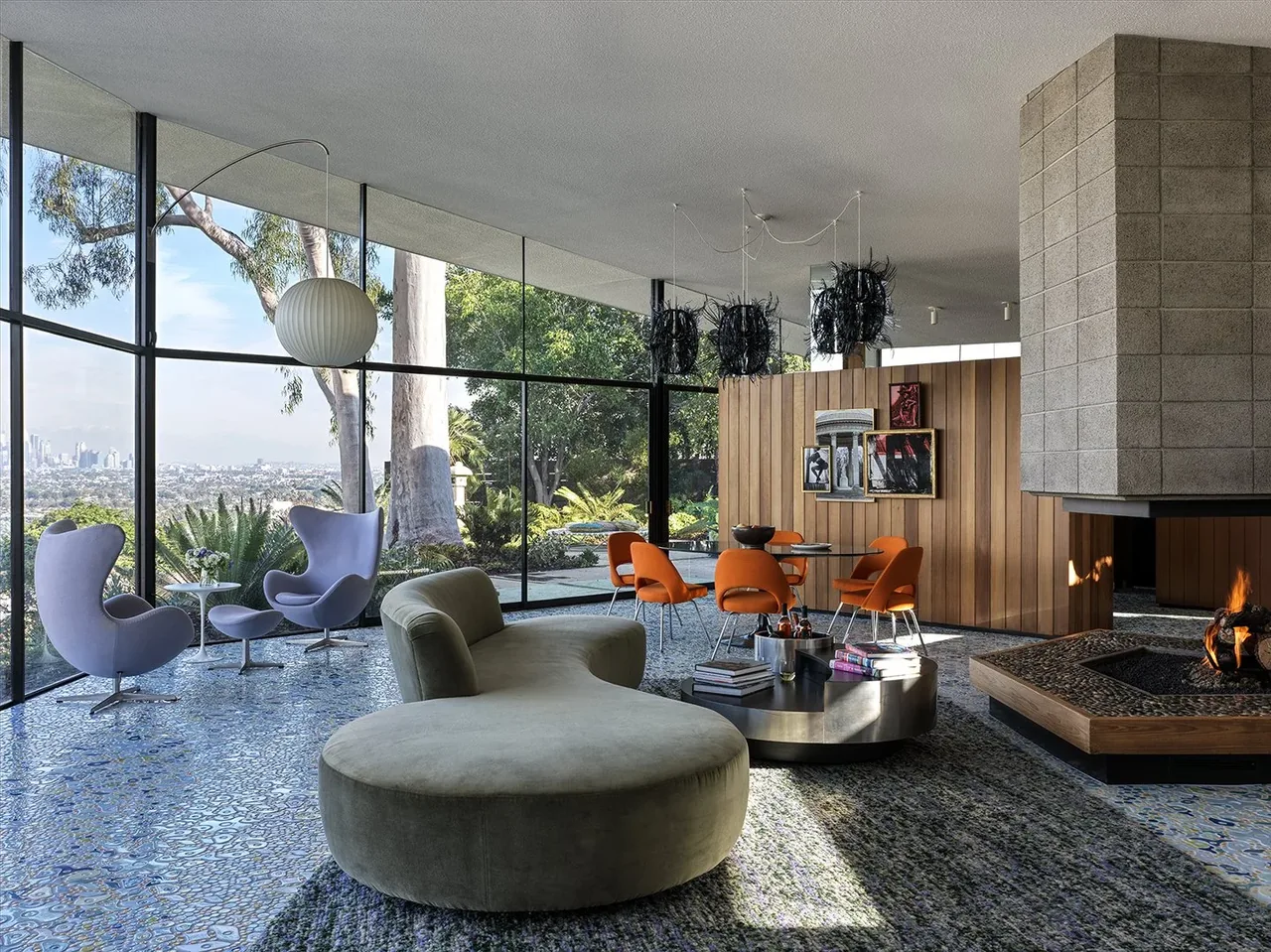 Living space with curved sofa and orange dining chairs adjacent to a wood-paneled wall and concrete block fireplace.
