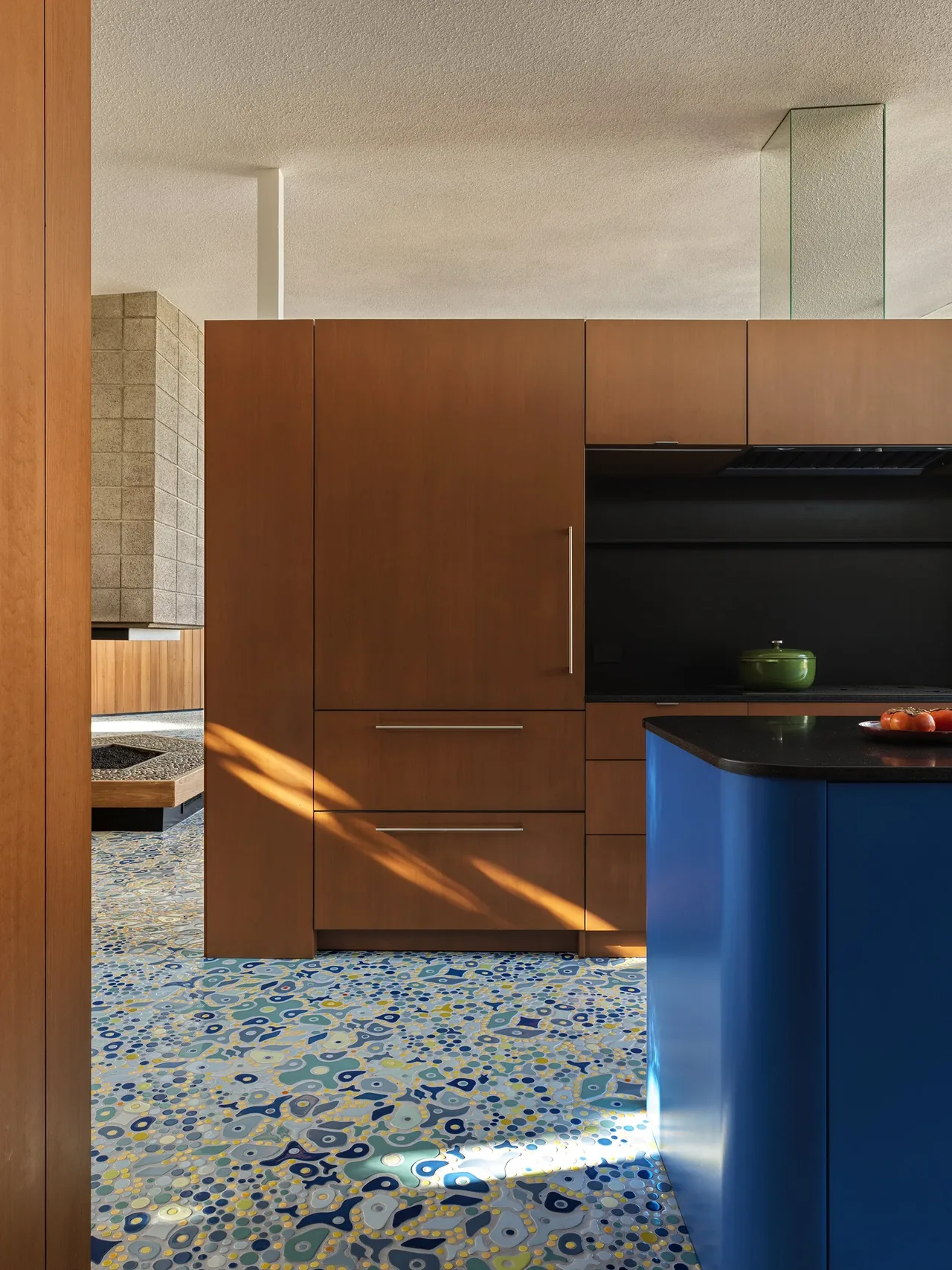 Kitchen featuring warm wood cabinetry, a blue island, and colorful terrazzo floor in the Baldwin Hills Vista project.
