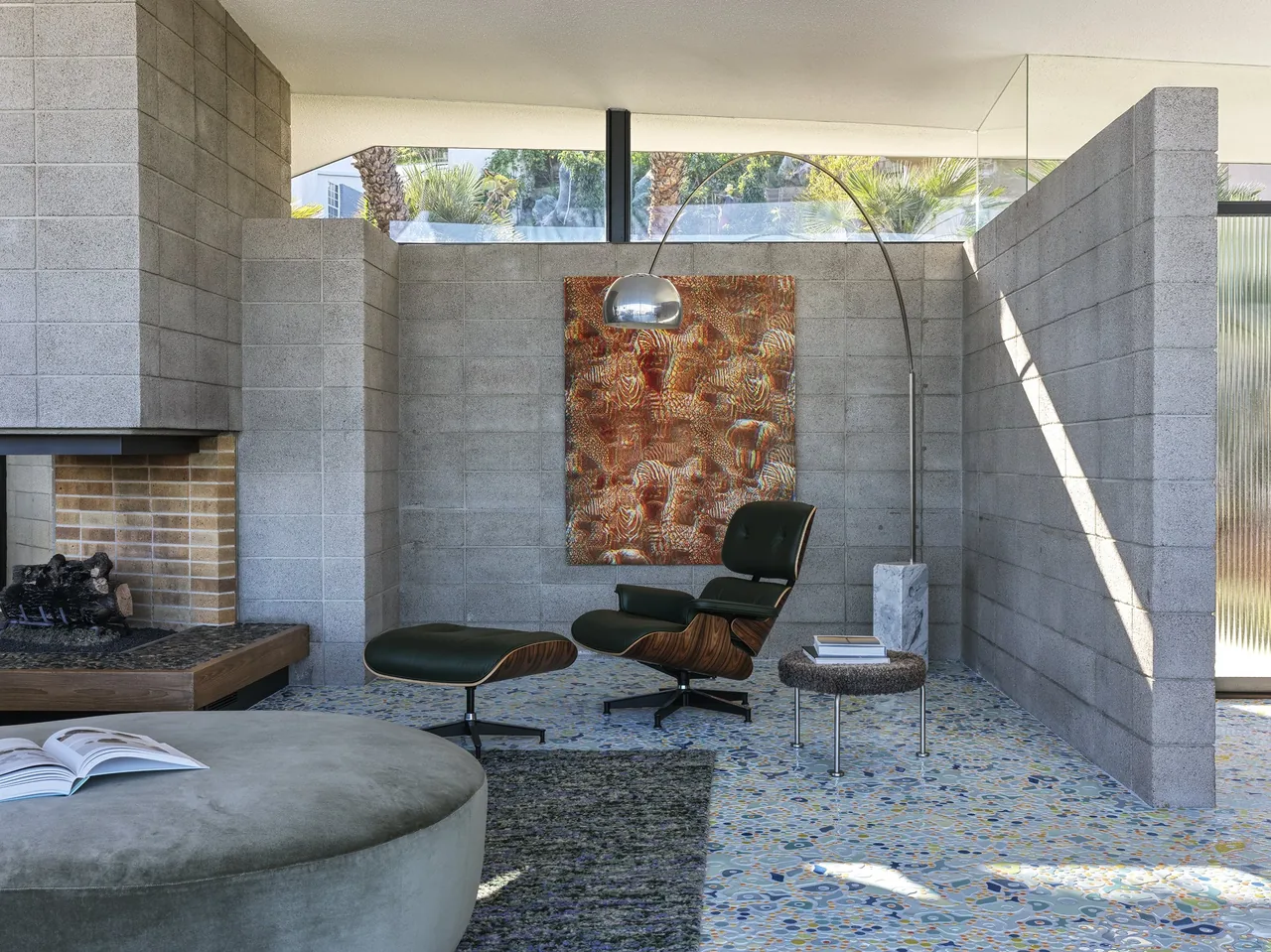 Living room features terrazzo flooring, a fireplace with brick interior, and a black lounge chair with ottoman under an arc floor lamp.