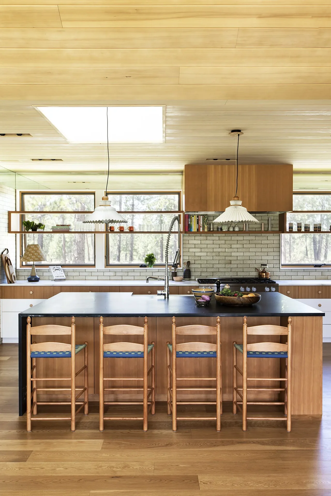 Kitchen interior of Bend House with wood cabinetry, black countertop island, and pendant lights over the island.