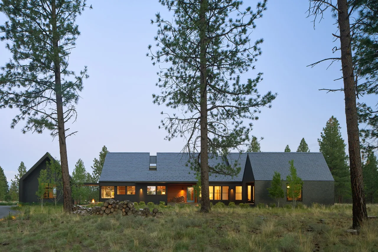 BEND HOUSE by Bestor Architecture features dark painted siding and sharp roof pitches amid natural grass landscape and pine trees.
