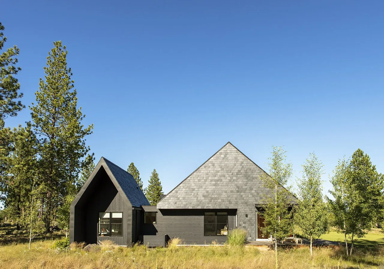 BEND HOUSE by Bestor Architecture features dark wood siding and sharply pitched rooflines amid a natural grass and tree landscape.