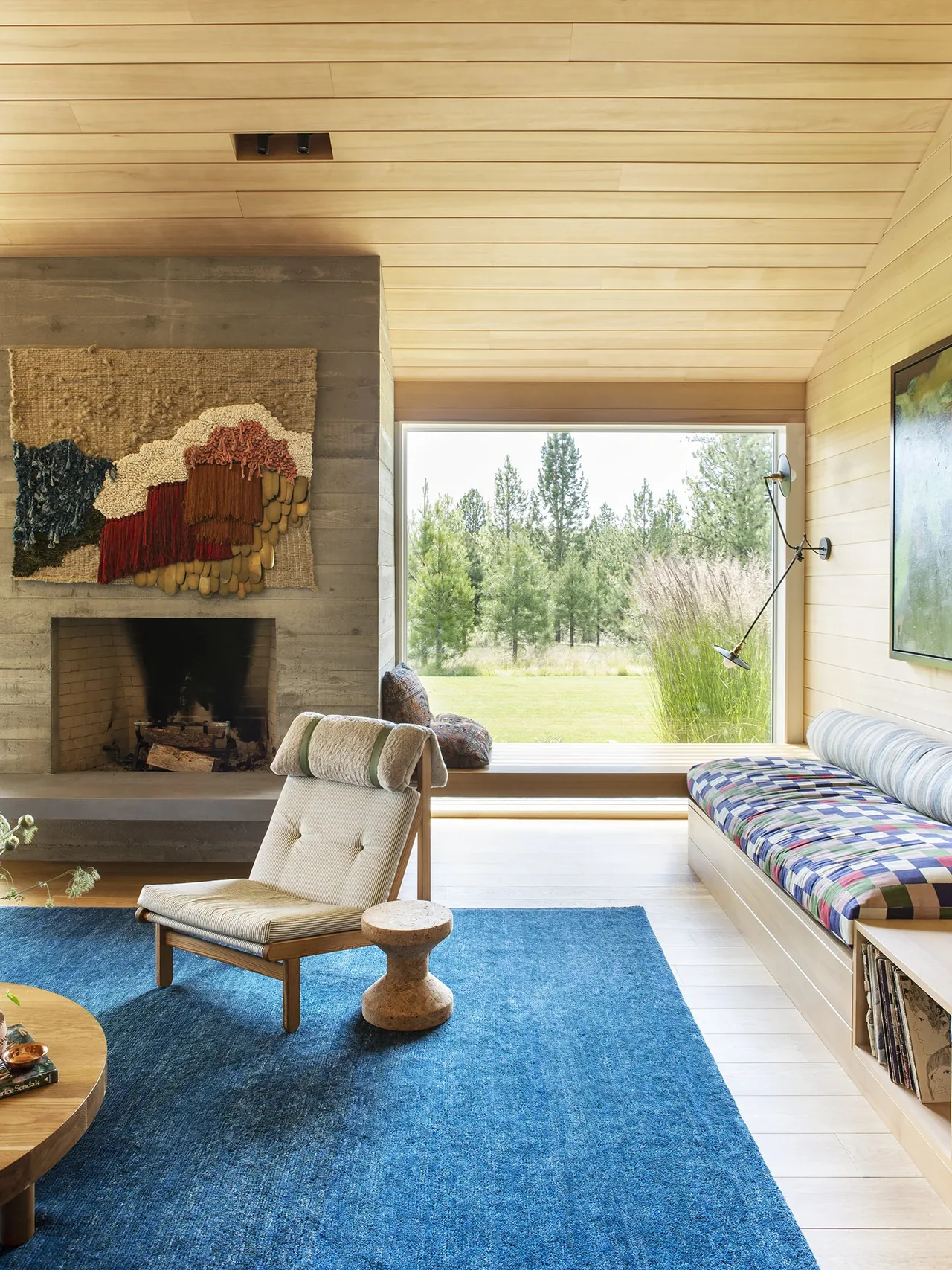 The BEND HOUSE living room features a concrete fireplace, wood-paneled vaulted ceiling, and a large window framing the outdoor landscape.