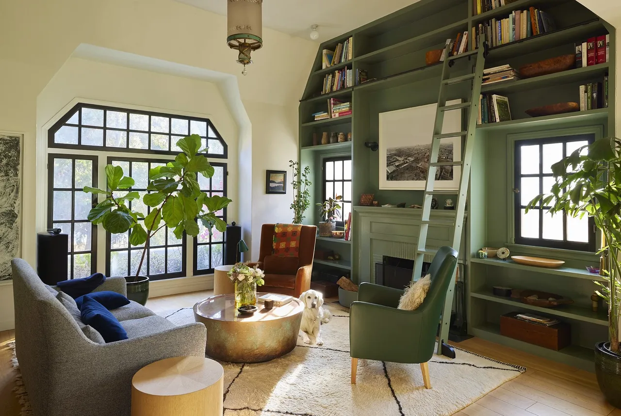 Living room with green built-in shelves around a fireplace, large black-framed window, and mixed seating.
