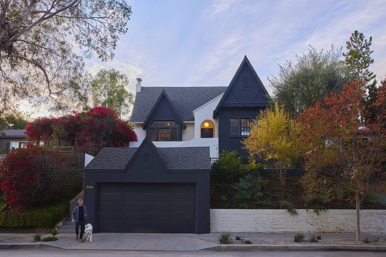 Two-tone Tudor home with dark garage and white upper walls, steep gable roofs, and mature landscaping.