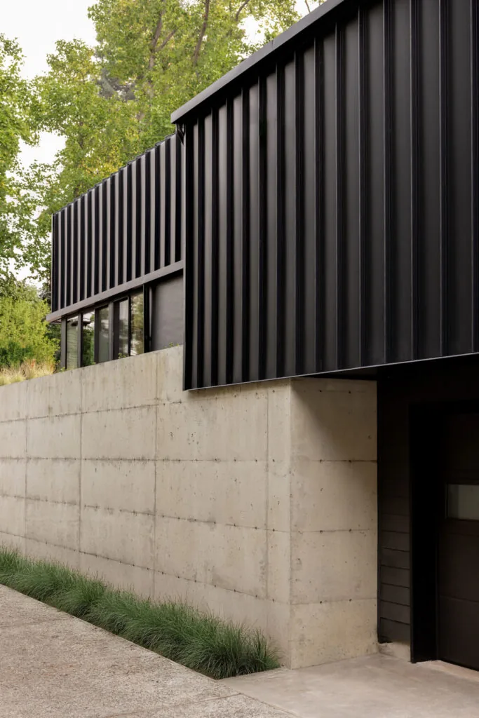 This exterior shows black vertical metal siding above a wood-grain textured concrete base wall.
