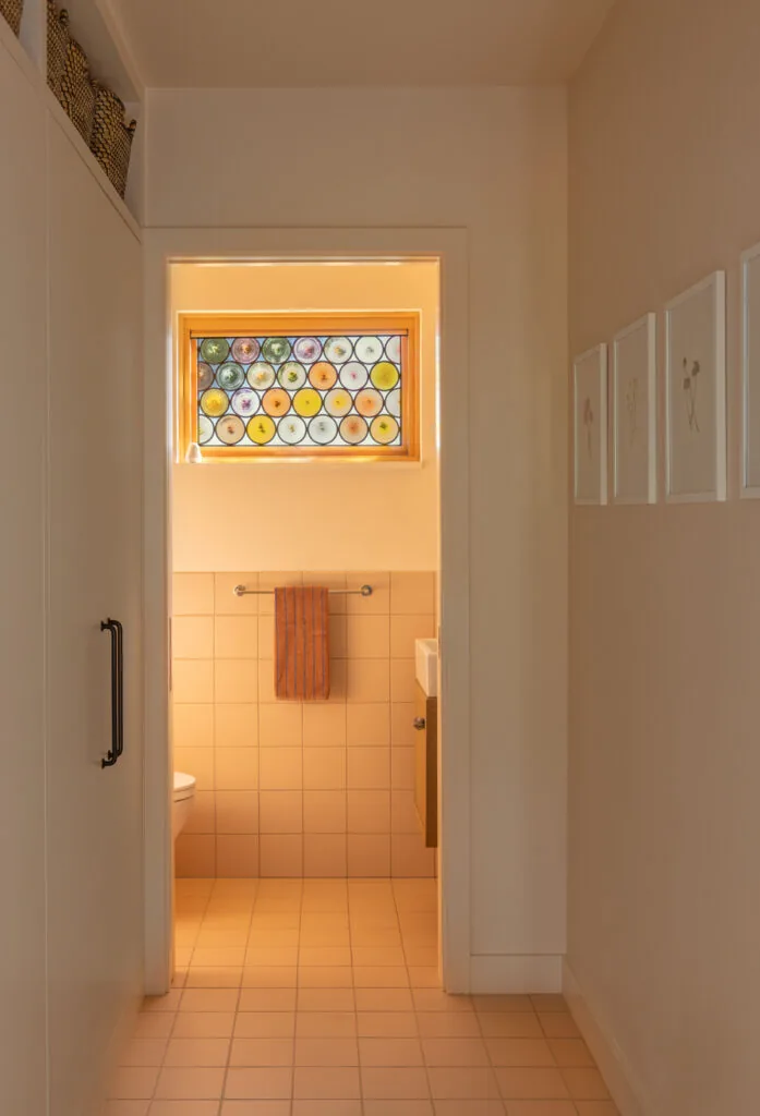 Bathroom with beige tile and a decorative circular stained glass window above the towel rack.