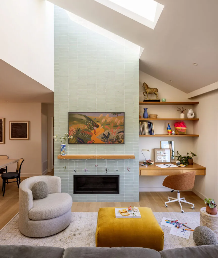 Living room features a light green tiled fireplace, built-in desk with shelves, and a skylight above for natural light.
