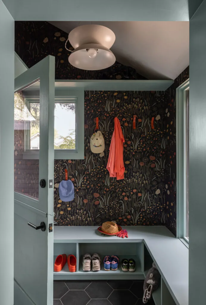 Mudroom with floral wallpaper and teal built-in bench having cubbies for shoe storage and coat hooks.