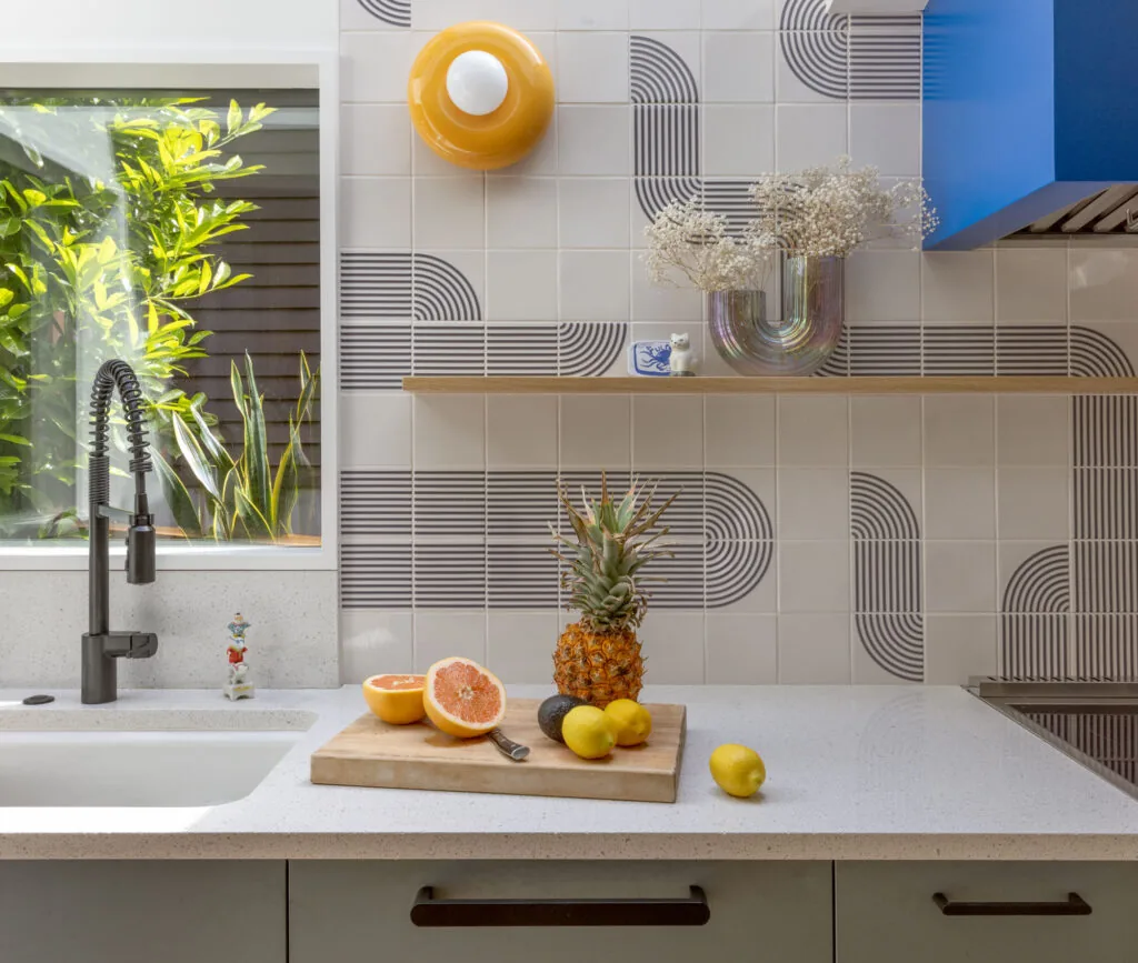 Kitchen countertop features white quartz, geometric tile backsplash, and a matte black spring kitchen faucet with blue cabinetry above.