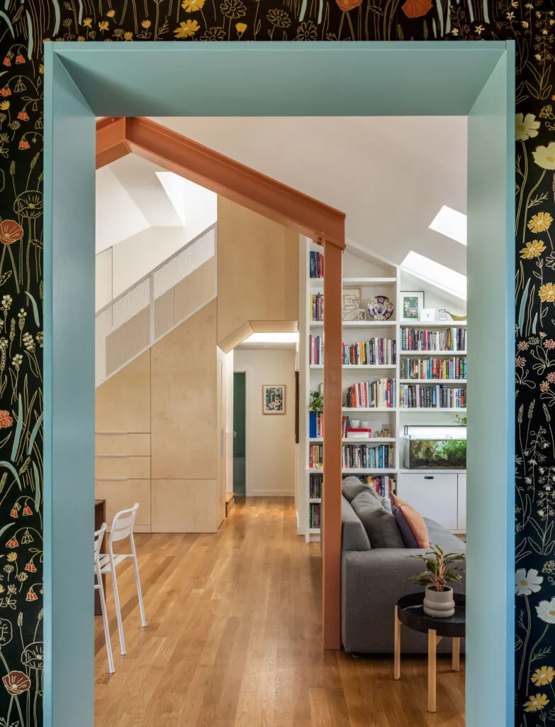 Interior view showing wood flooring, built-in shelving and stairs, and a gray sofa in a light-filled living space.