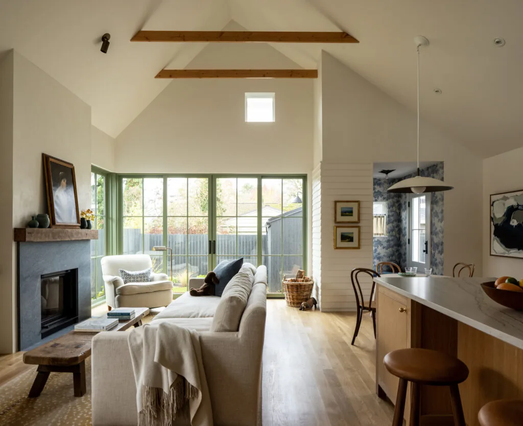 Rad Trad living area features vaulted ceilings with exposed beams and green window frames around large glass doors.