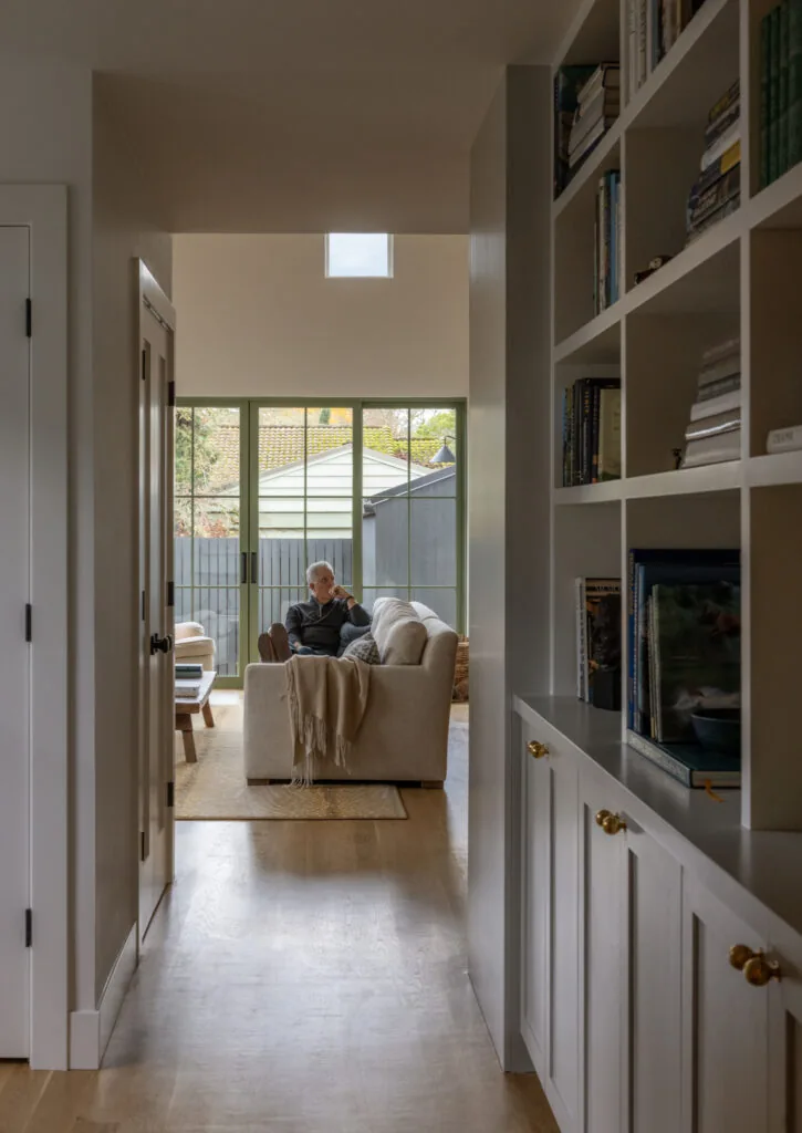 Living room with beige sofa and green-framed sliding glass doors visible from hallway with built-in shelves.