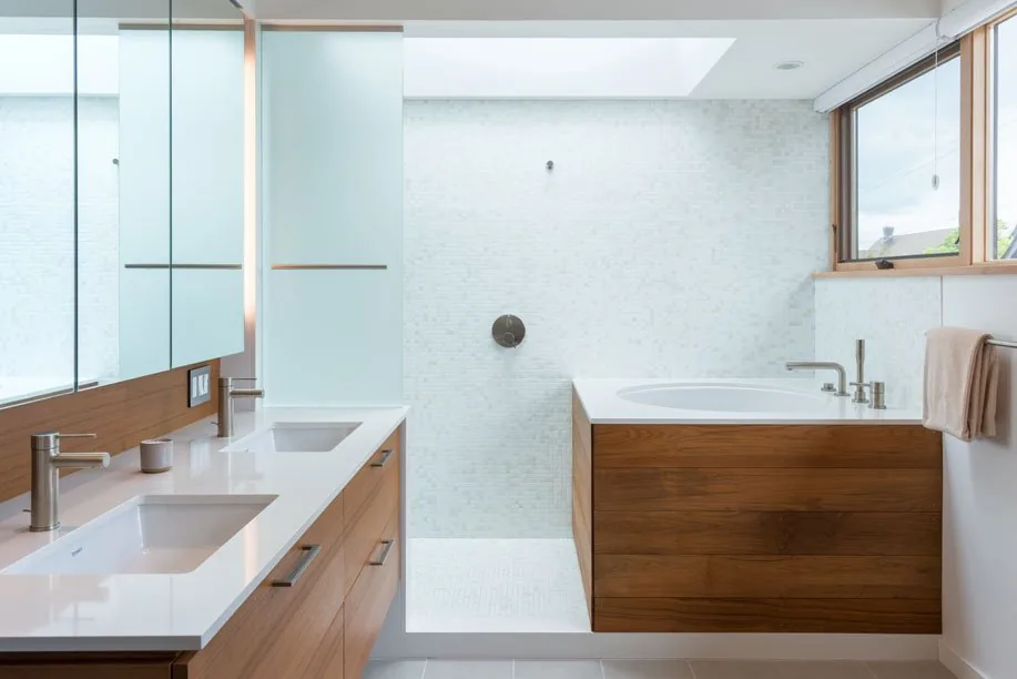 This bathroom features a wooden vanity with dual sinks, a wood-clad bathtub, and a walk-in shower with white mosaic tiles under a skylight.