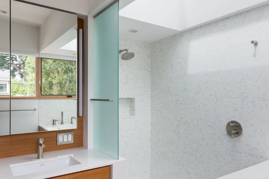 This bathroom features a white tile shower with a frosted glass partition and a wood vanity with undermount sink.