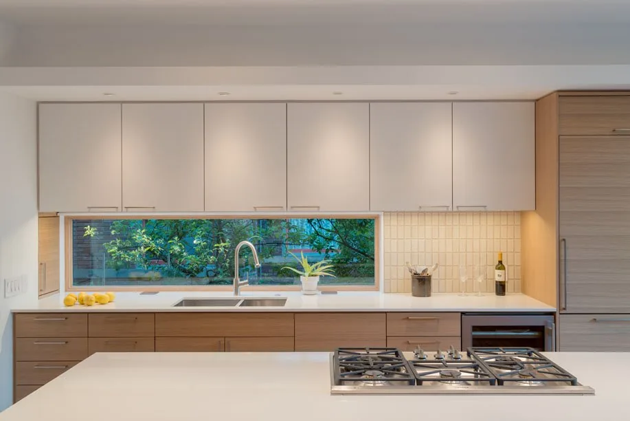 Kitchen with a horizontal window above the sink, white upper cabinets, wood lower cabinets, and gas cooktop on the island.