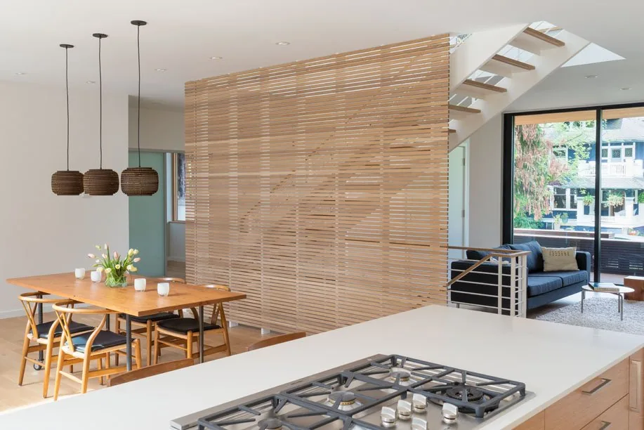 Dining area with wood table and chairs separated from living room by wood slat wall; large sliding glass door opens to outdoor space.