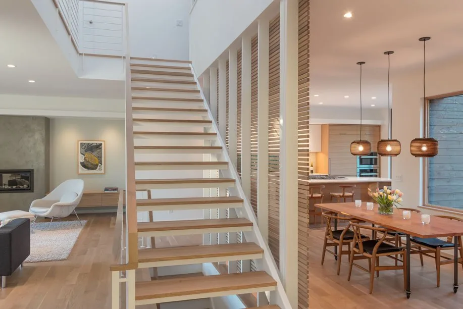Open riser staircase separates dining and living rooms in the Capitol Hill Residence with wood flooring and pendant lamps.