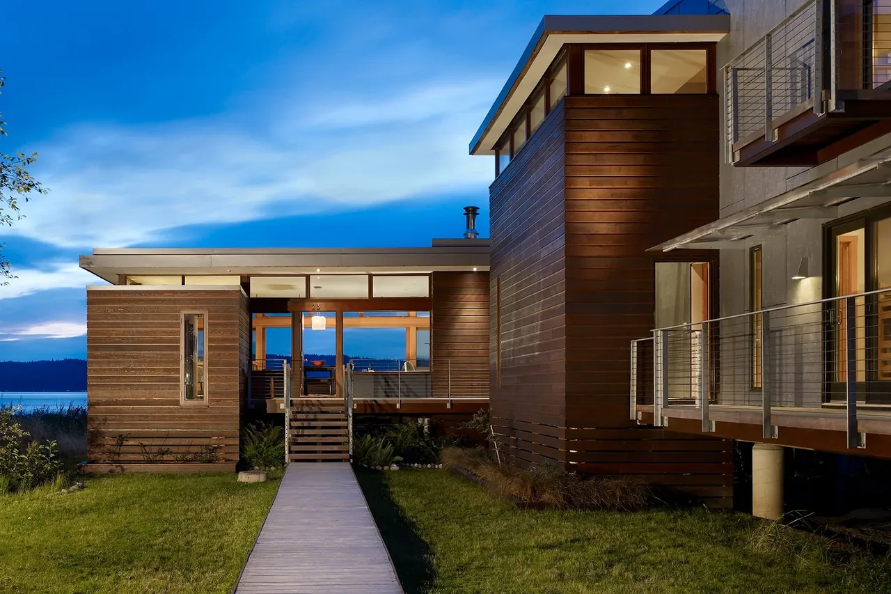 Hat Island Residence by Serra Wersinger Architects features horizontal wood siding and expansive glazing overlooking a waterfront landscape.