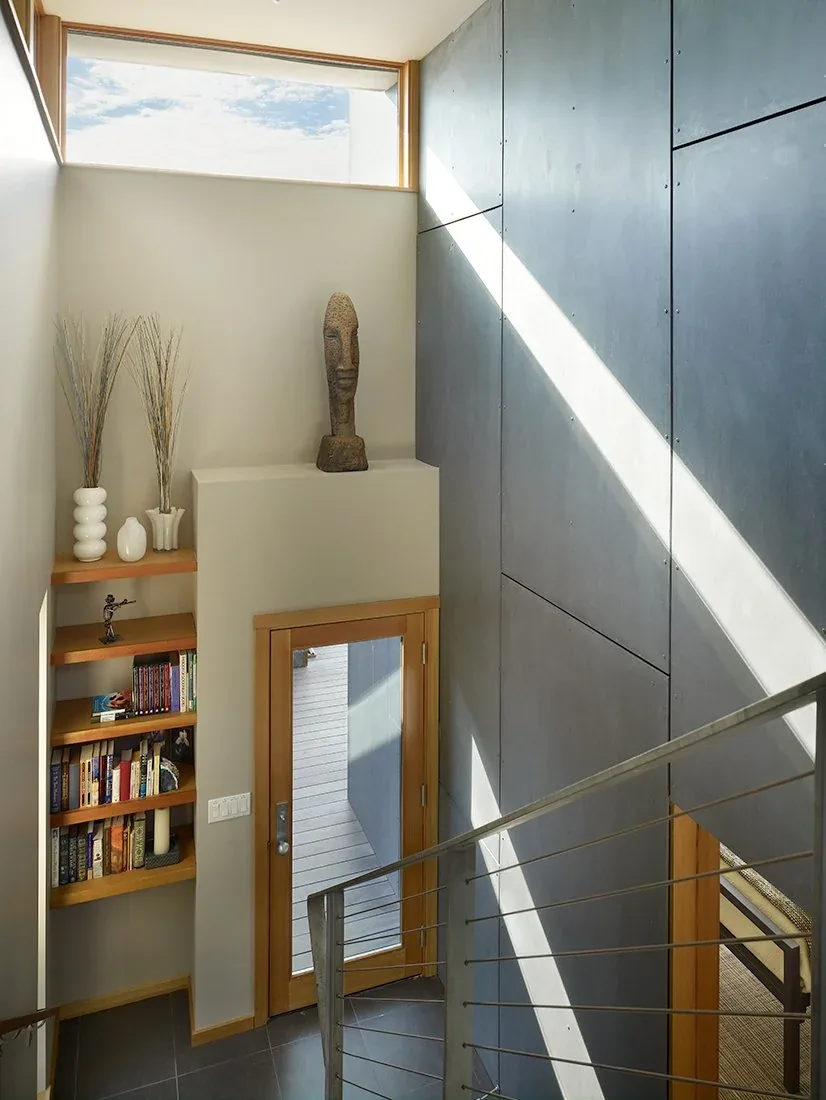 Interior stairwell featuring metal railing, built-in wood shelves, and a tall horizontal window above the entry door.