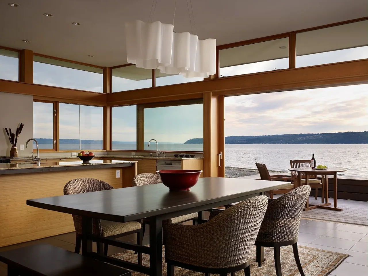 Dining and kitchen with wood trim and large windows offer expansive water views and access to an outdoor dining deck.
