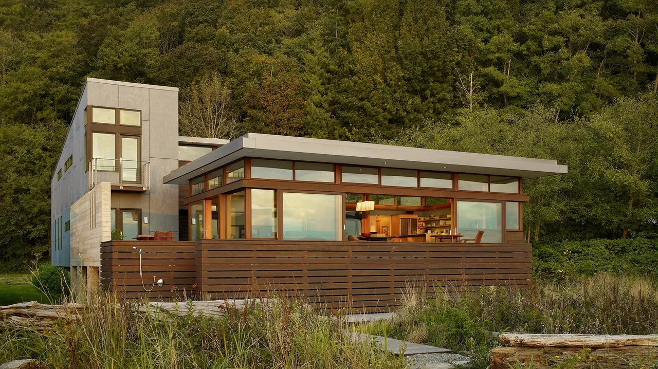Hat Island Residence features a flat roof and large wood-framed windows with a wood privacy fence on the exterior.