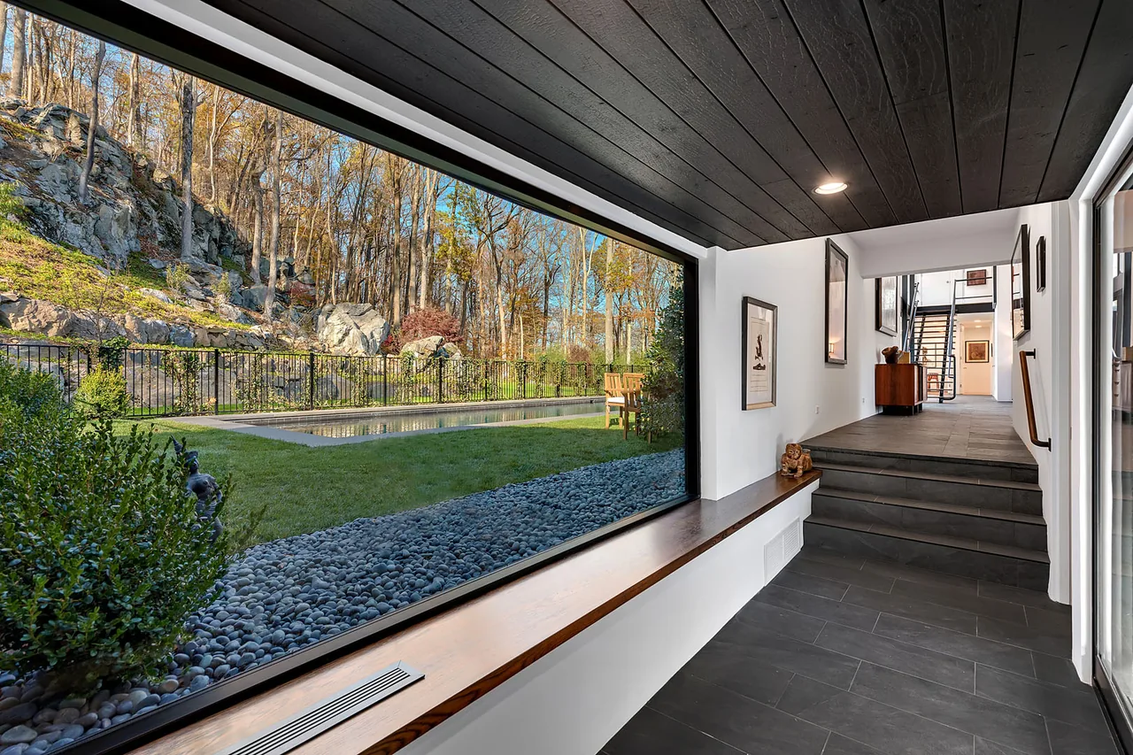 A corridor with large picture window overlooks the pool and rocky landscape at the Stockwell-Rodríguez Residence by Belmont Freeman Architects.