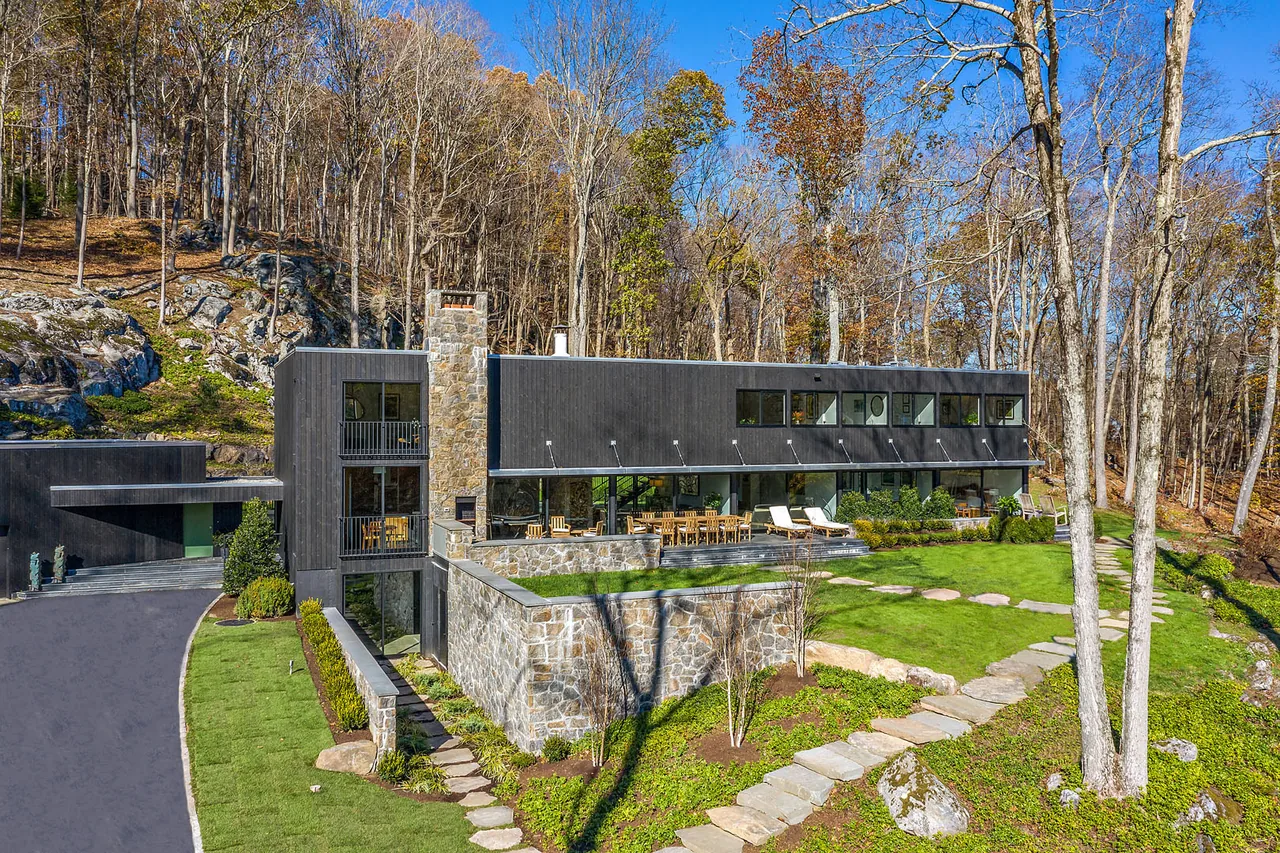 Stockwell-Rodríguez Residence by Belmont Freeman Architects features dark wood siding and stone elements on a rocky hillside.