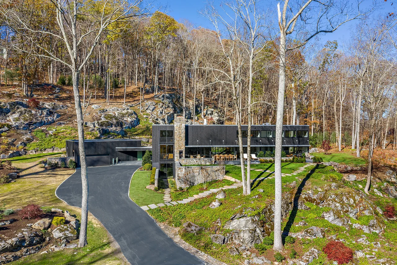 The Stockwell-Rodríguez Residence features black stained wood siding and a stone chimney, nestled on a rocky hillside.
