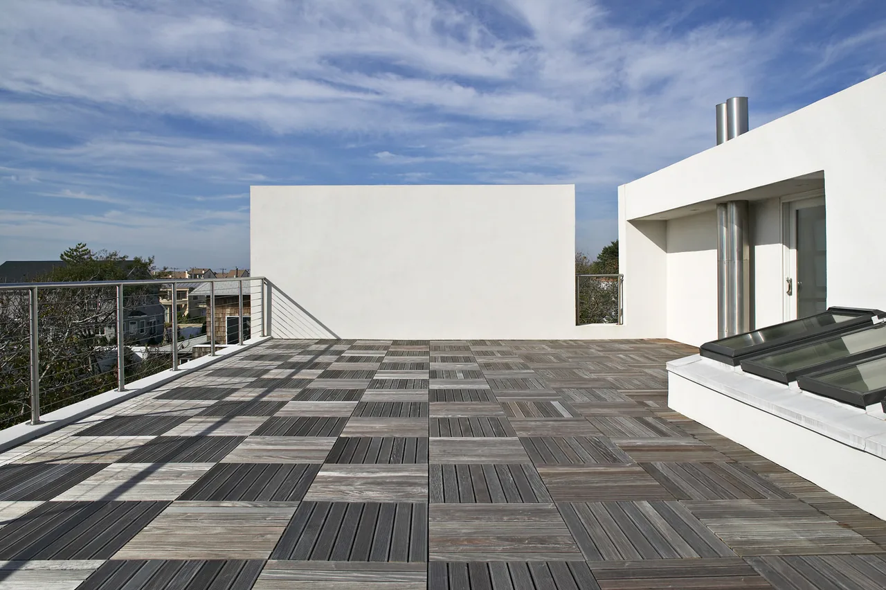 Rooftop deck featuring checkered wood flooring and stainless steel railing with a view over nearby houses.