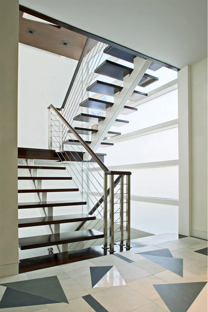 The Kowalewski Residence features a floating staircase with dark wood treads and metal railings against a frosted glass window wall.