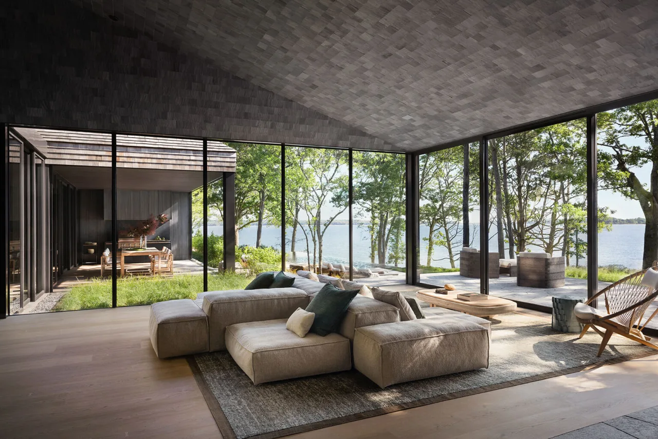 Sag Harbor Bay living room features floor-to-ceiling glass walls framing a waterfront view and adjacent outdoor spaces.