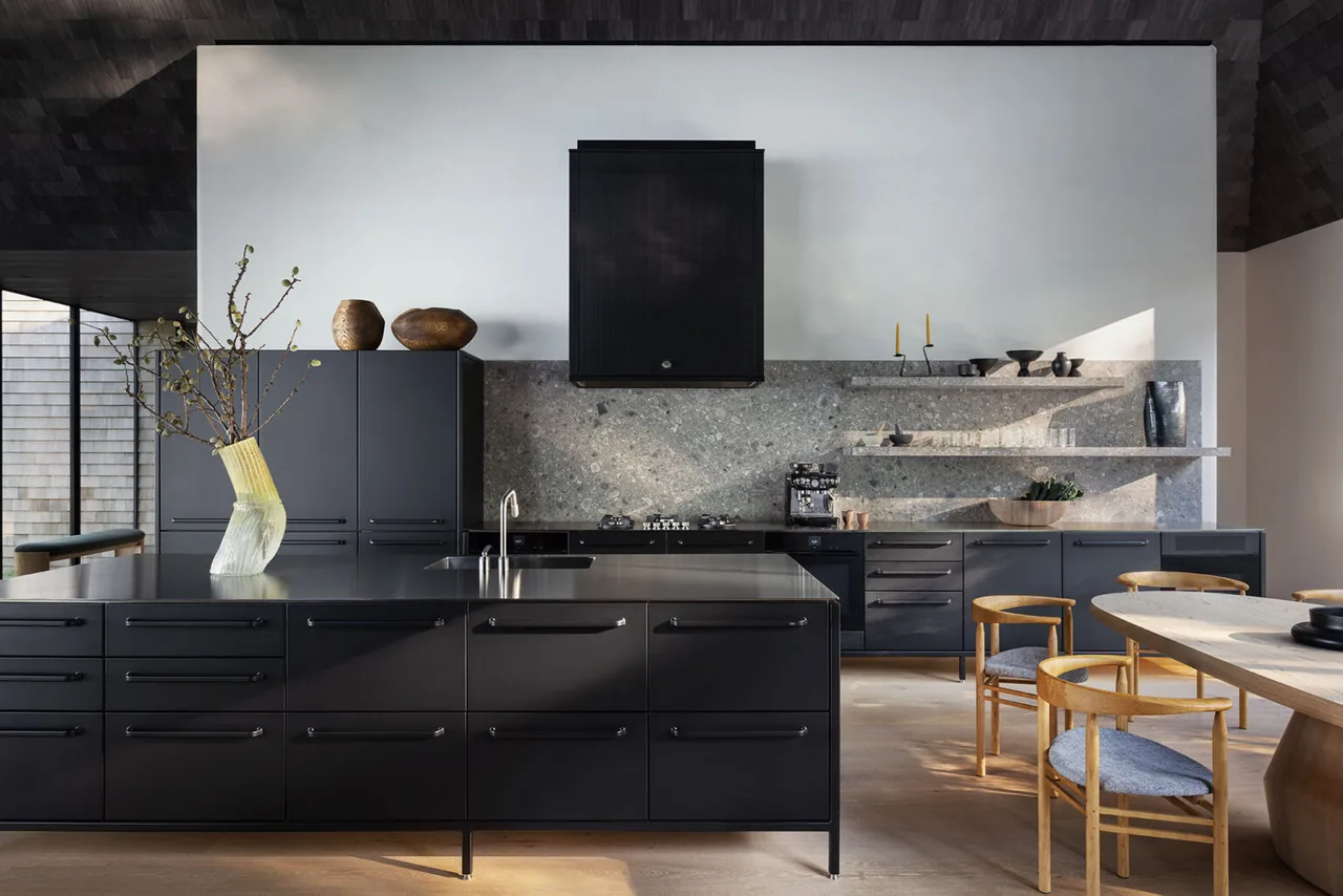 Sag Harbor Bay features a modern kitchen with black cabinetry, stone backsplash, and wood dining furniture.