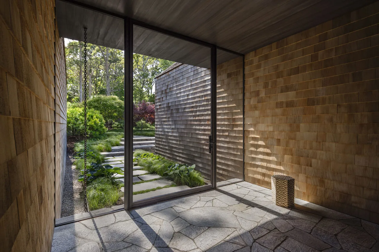 Entryway of Sag Harbor Bay project featuring wood shingle siding and stone pathway visible through glass door.