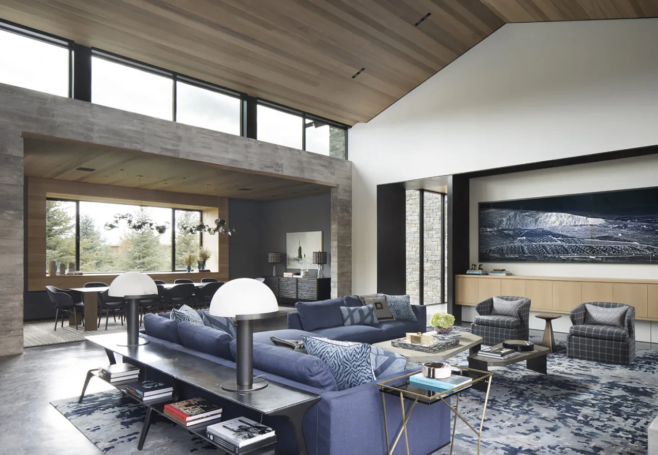 Living room with vaulted ceiling features blue sofas, plaid armchairs, and a large artwork above a wood cabinet.
