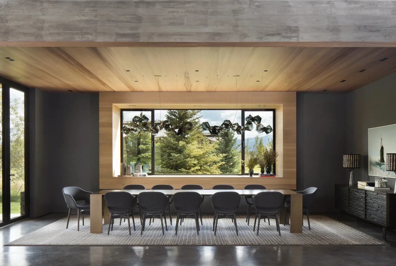 Shooting Star dining room features a long table, black chairs, patterned rug, and a large wood-framed window to natural greenery.
