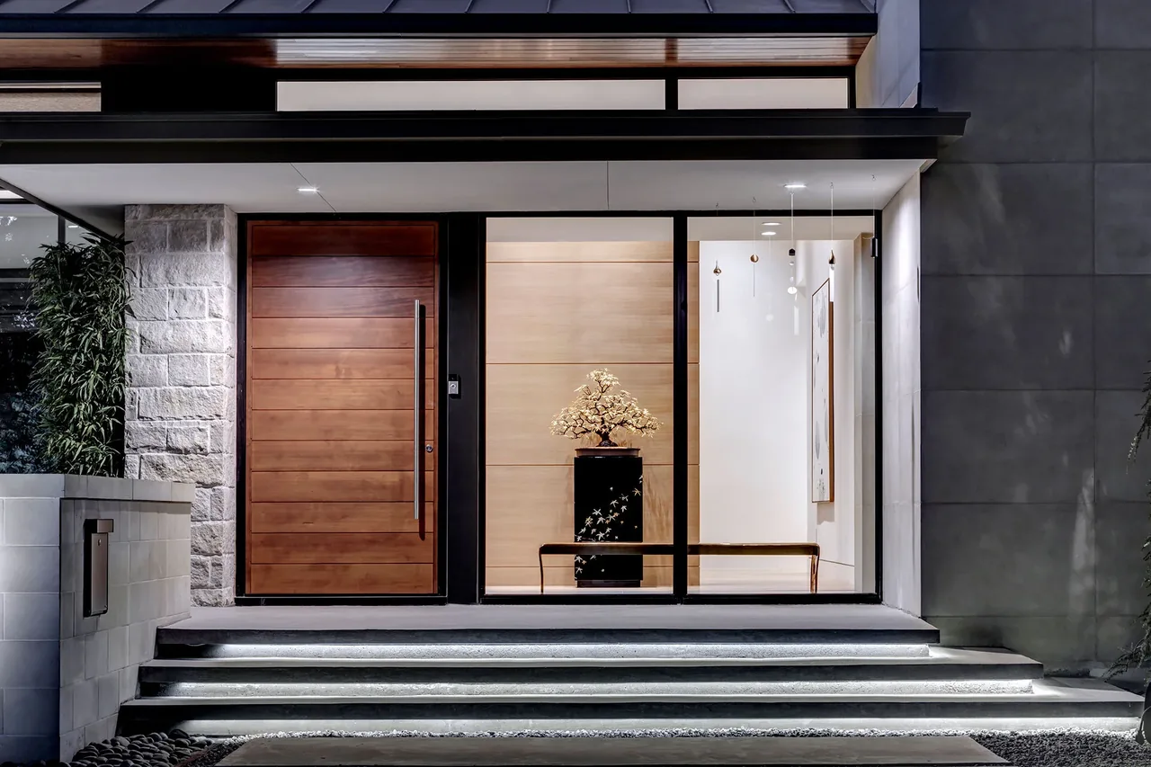 The Manning project entrance features a large wood door, floor-to-ceiling glass panel, and illuminated stepped pathway.