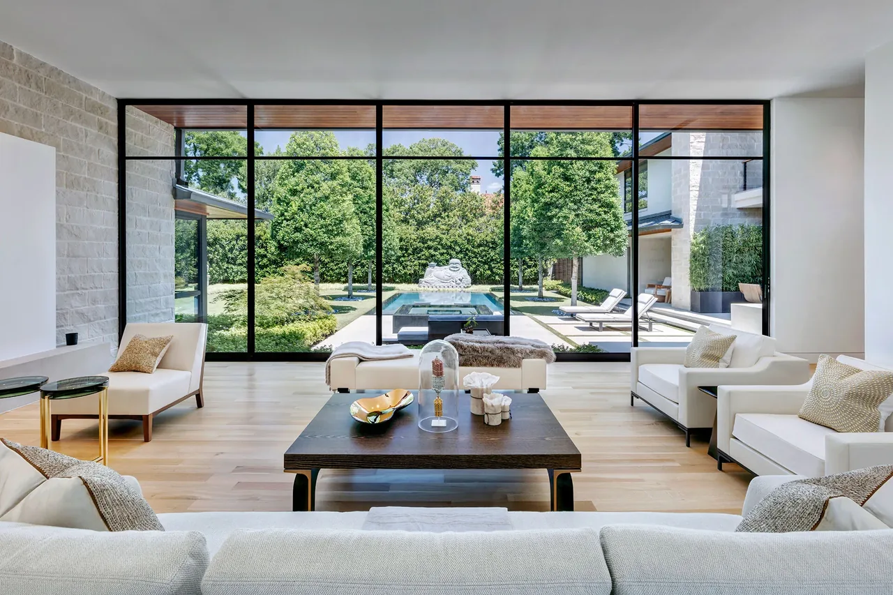 Living room features large black window frames opening to a landscaped garden with pool and floral sculpture.
